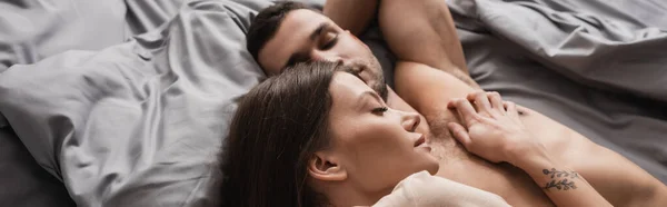 Vista dall'alto della donna sdraiata vicino al fidanzato muscoloso senza maglietta sul letto, banner — Foto stock