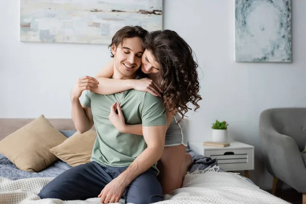 Mujer rizada abrazando novio feliz con los ojos cerrados - foto de stock