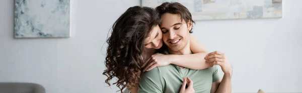 Mujer rizada abrazando novio feliz con los ojos cerrados, bandera - foto de stock
