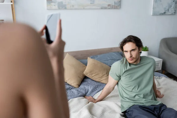 Mujer joven borrosa tomando fotos de novio en el dormitorio - foto de stock