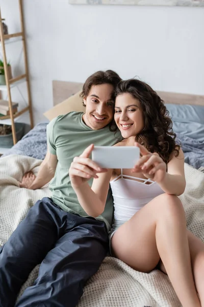 Femme bouclée et homme heureux prenant selfie dans la chambre — Photo de stock