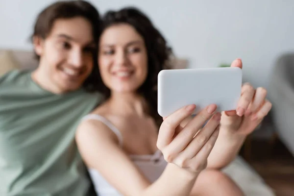 Blurred curly woman and happy man taking selfie in bedroom — Stock Photo