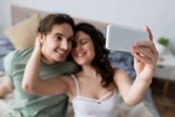 Coppia offuscata e felice prendendo selfie in camera da letto — Foto stock