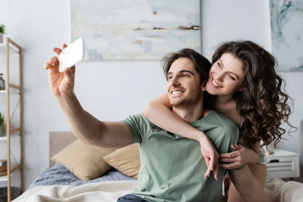 Feliz joven pareja tomando selfie en dormitorio - foto de stock