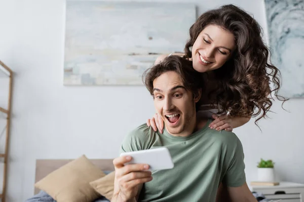 Uomo e donna stupiti guardando smartphone a casa — Foto stock