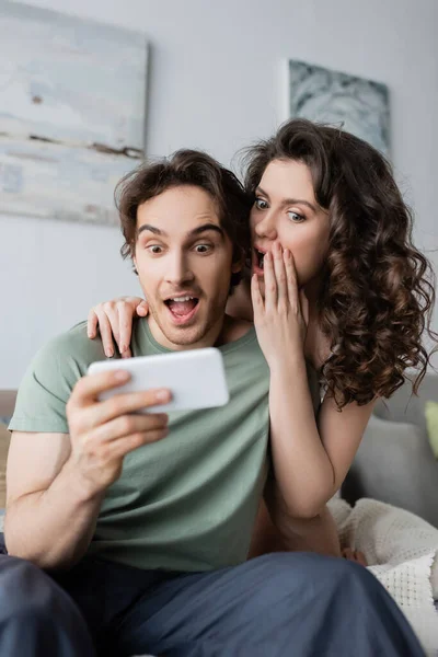 Sorprendido hombre y mujer mirando el teléfono inteligente en casa - foto de stock