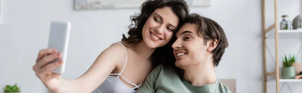 Alegre y joven pareja tomando selfie en casa, bandera - foto de stock