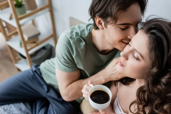 Високий кут зору щасливого чоловіка цілує кучеряву дівчину з чашкою кави — стокове фото