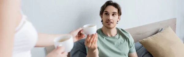 Blurred woman giving cup of coffee to boyfriend in bed, banner — Stock Photo