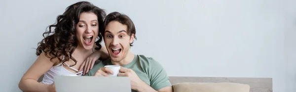 Pareja joven emocionada mirando el ordenador portátil en el dormitorio, pancarta - foto de stock