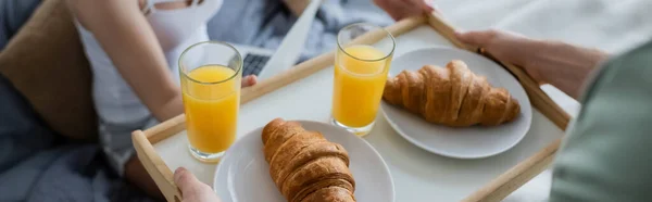 Vista recortada del hombre tatuado sosteniendo bandeja con sabroso desayuno cerca de la novia en la cama, pancarta - foto de stock