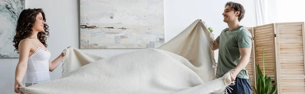 Vista lateral de casal jovem sorridente segurando cobertor, banner — Fotografia de Stock