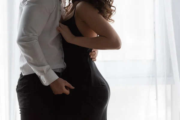 Vista recortada de la mujer apasionada en vestido de deslizamiento desabotonar camisa de hombre — Stock Photo