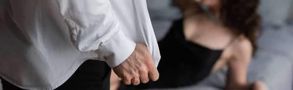 Abgeschnittene Ansicht eines Mannes, der sein weißes Hemd auszieht, neben einer verschwommenen Frau auf dem Bett, Banner — Stockfoto