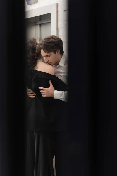 Hombre en camisa blanca besando hombro de mujer seductora cerca del ascensor - foto de stock