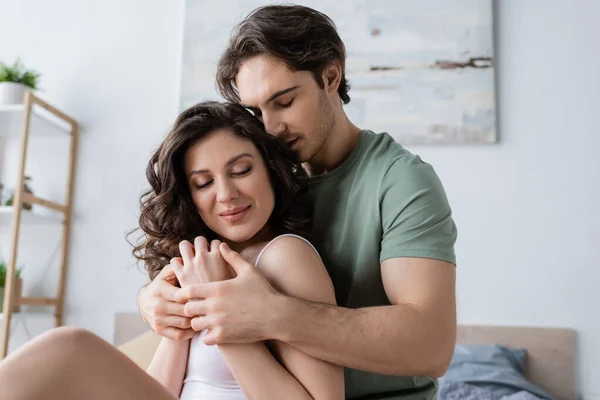 Hombre en camiseta verde abrazando a la mujer sonriente en casa - foto de stock