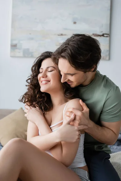 Hombre en camiseta verde abrazando a la mujer feliz en casa - foto de stock