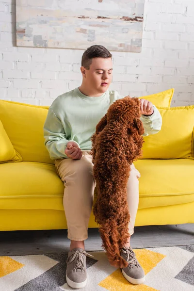 Teenager with down syndrome playing with brown poodle at home — Stock Photo