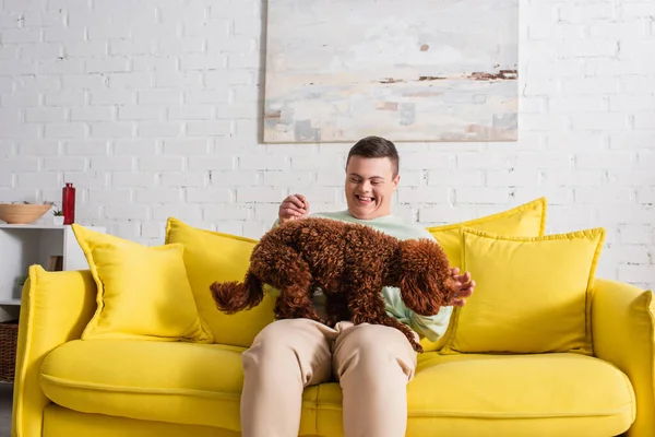 Positive teenager with down syndrome playing with brown poodle in living room — Stock Photo