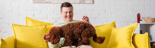 Glücklicher Junge mit Down-Syndrom spielt mit Pudel auf Couch, Banner — Stockfoto