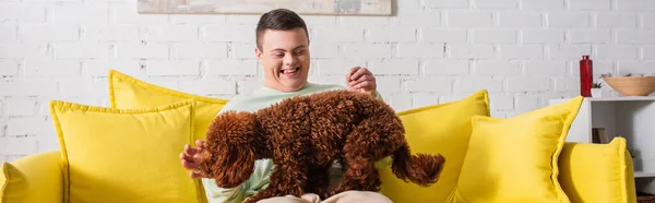 Happy boy with down syndrome playing with poodle on couch, banner — Stock Photo