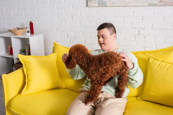 Teen boy with down syndrome playing with poodle on couch — Stock Photo