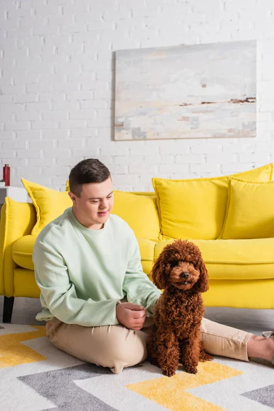 Adolescente com síndrome de down olhando para poodle no chão em casa — Fotografia de Stock