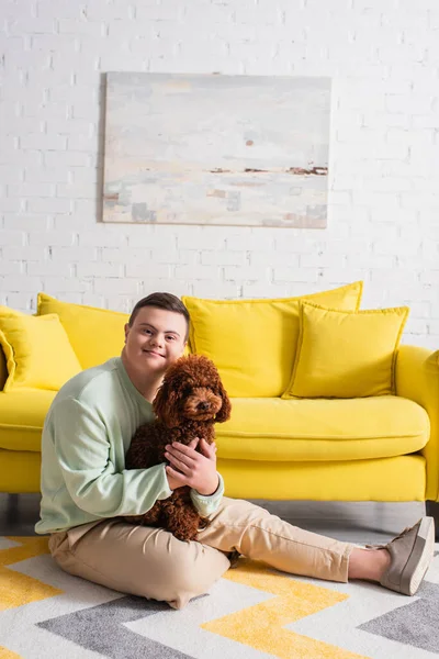 Heureux adolescent garçon avec le syndrome du duvet étreignant caniche dans le salon — Photo de stock