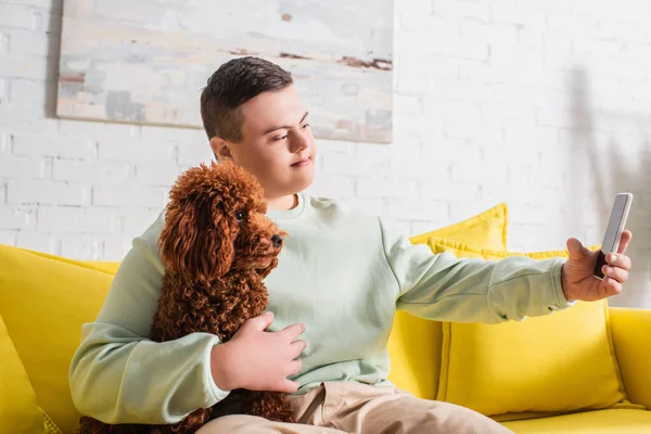 Adolescent garçon avec vers le bas syndrome prendre selfie avec caniche à la maison — Photo de stock