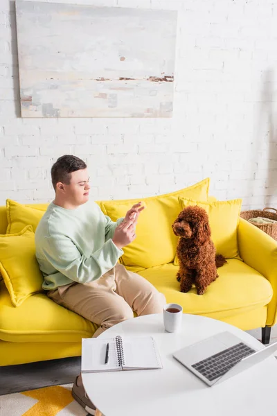 Teenager with down syndrome taking photo of poodle near tea and laptop on table — Stock Photo