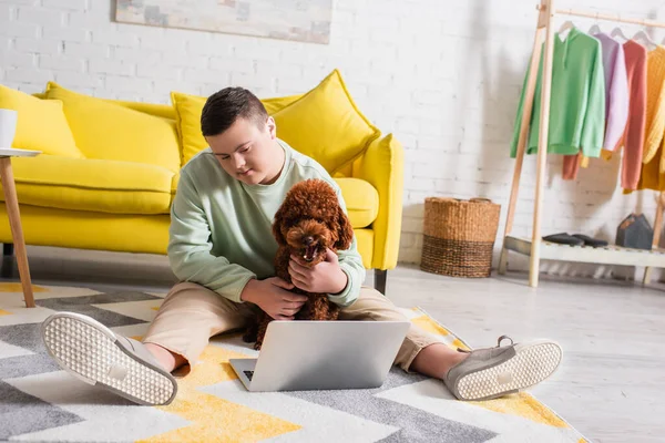 Adolescente com síndrome de down poodle de estimação perto de laptop no chão em casa — Fotografia de Stock