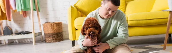 Adolescente com síndrome de down acariciando poodle marrom no chão em casa, banner — Fotografia de Stock