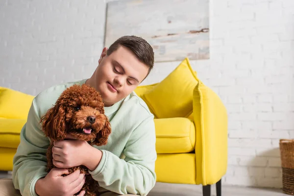 Jeune garçon avec le syndrome du duvet étreignant caniche brun à la maison — Photo de stock