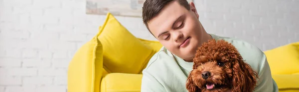 Teenager with down syndrome looking at brown poodle at home, banner — Stock Photo