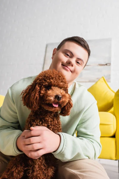 Teen boy with down syndrome hugging poodle and looking at camera in living room — Stock Photo