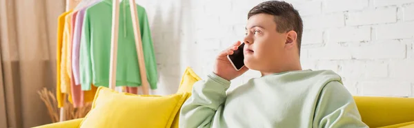 Teenager with down syndrome talking on smartphone on couch at home, banner — Stock Photo