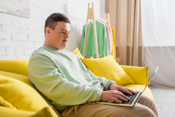 Підліток з синдромом Дауна використовує ноутбук на дивані вдома — стокове фото