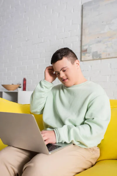 Підліток з синдромом Дауна використовує ноутбук на дивані у вітальні — стокове фото