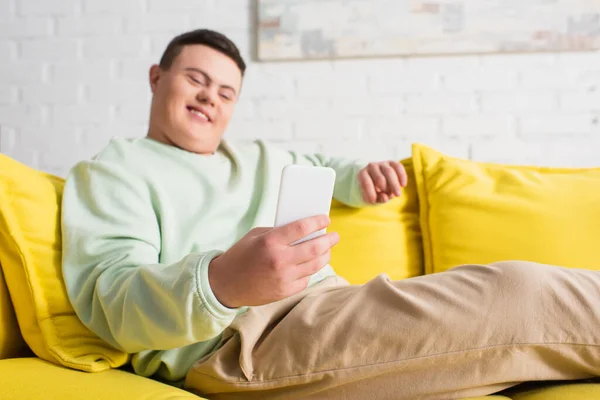 Smartphone in hand of blurred teenager with down syndrome on couch — Stock Photo