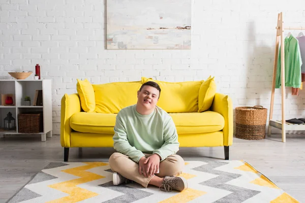 Positive teenager with down syndrome sitting on floor at home — Stock Photo