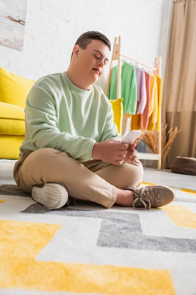 Vista a basso angolo di adolescente con sindrome di Down utilizzando smartphone sul pavimento a casa — Foto stock