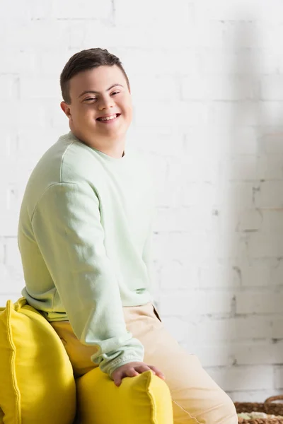 Positive teenager with down syndrome looking at camera near couch in living room — Stock Photo