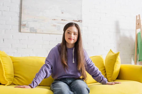 Lächelndes Teenager-Mädchen mit Down-Syndrom sitzt zu Hause auf der Couch — Stockfoto