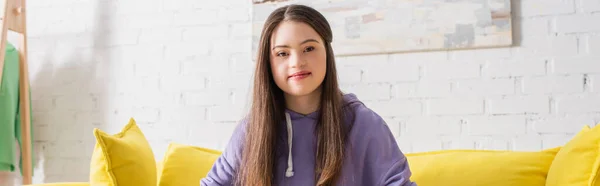 Positives Teenager-Mädchen mit Down-Syndrom schaut auf Couch zu Hause in die Kamera, Banner — Stockfoto