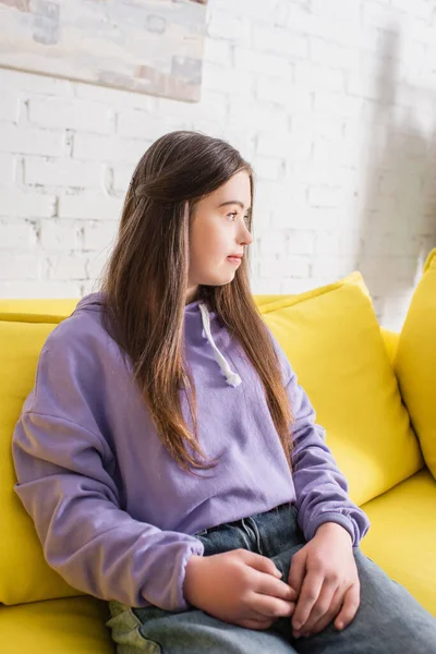 Вид збоку дівчини-підлітка з синдромом Дауна, що сидить на дивані вдома — стокове фото