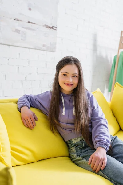 Glückliches Mädchen mit Down-Syndrom schaut auf Couch im Wohnzimmer in die Kamera — Stockfoto