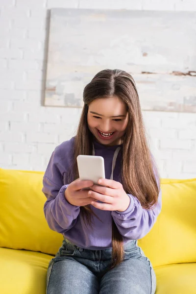 Menina adolescente positiva com síndrome de down usando celular na sala de estar — Fotografia de Stock