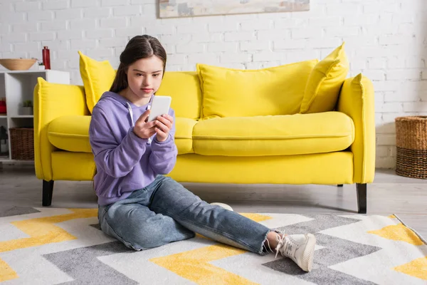 Teen girl with down syndrome using smartphone on floor at home — Stock Photo