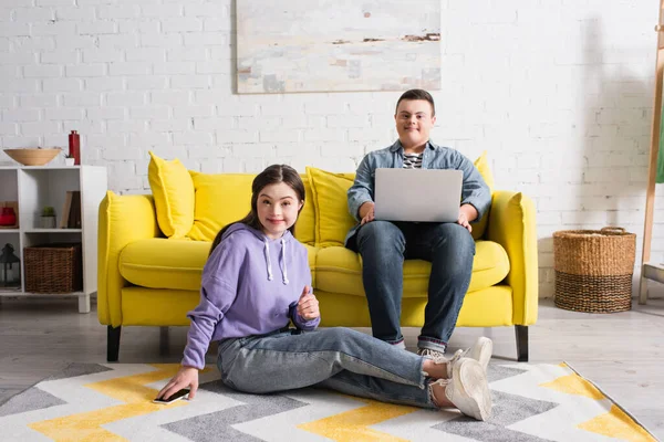 Positive teenagers with down syndrome looking at camera near devices at home — Stock Photo