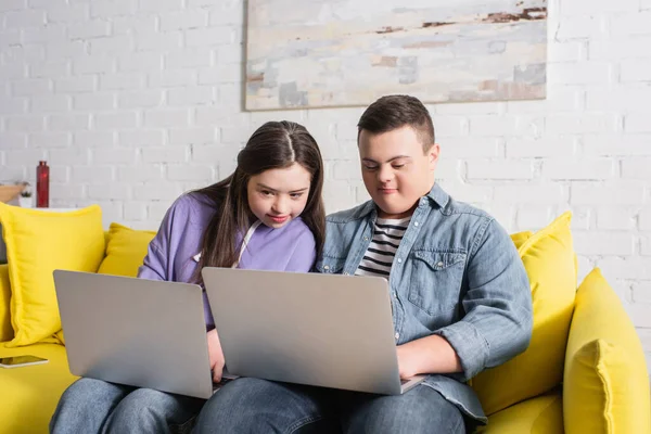 Adolescentes com síndrome de down usando laptops no sofá em casa — Fotografia de Stock